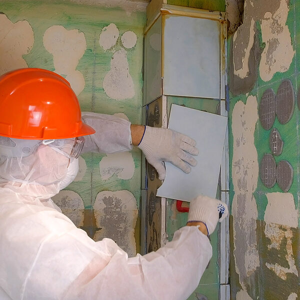 Man tiler making renovation repair at home, removes tiles from wall in toilet using tool red crowbar. Construction works. Unrecognizable builder wearing in uniform and safety helmet.